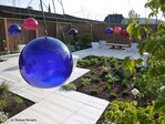 Der Entwurf “Le jardin mange-tête (Der Kopffressergarten) spielt mit nach unten offenen Farbkugeln, die an Metallgestellen hängen. Er fordert dazu auf, mit dem Kopf in die transparenten Glocken einzutauchen und den überwiegend weißen Garten in farbigem Licht zu sehen, aber auch die eigene Stimme zu hören. Starr stehend mit Kopfschmuck erscheinen die Besucher wie “Raumfahrer“, sitzend wie beim Frisör unter der Trockenhaube. Die Designer nennen ihre Versuchsanordnung ein Landschaftsexperiment „participio-chromatique.“ (th)