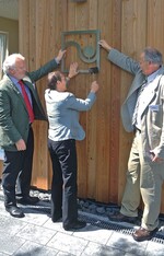 Anja Hajduk beim Anbringen des GaLaBau-Emblems – Thomas Schmale (l.) und Hanns-Jürgen Redeker helfen