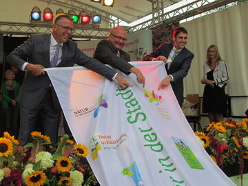 (v.l.) Franz Stahl, Erster Brgermeister der Stadt Tirschenreuth, und Roland Albert, Vorsitzender der Gesellschaft zur Frderung der bayerischen Landesgartenschauen mbH bergeben die Gartenschau-Fahne an den Brgermeister der Stadt Alzenau, Dr. Alexander Legler.