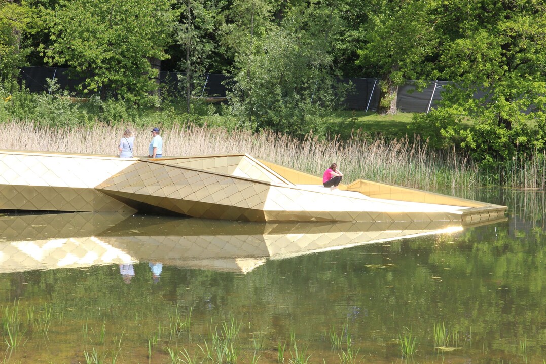 Die goldene Seerose markiert das sdliche Ende des Weiherstegs, der sich mit seiner goldenen Gestaltung auffllig durch den Klingenweiherpark zieht als prgendes gestalterisches Element.